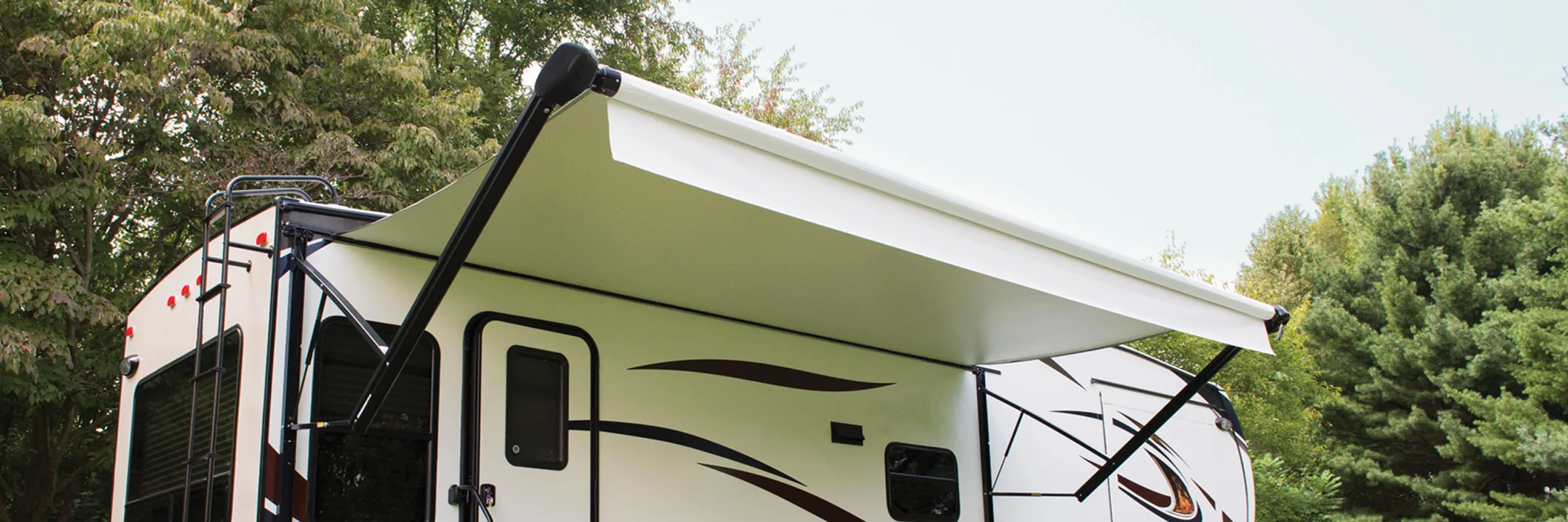Travel trailer with its awning extended at a wooded campsite