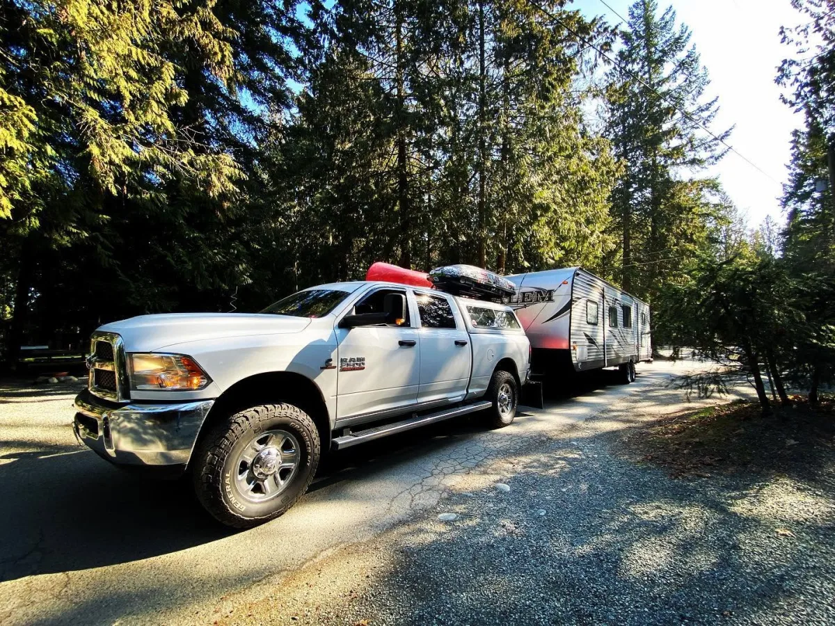 Pickup truck towing a travel trailer through a wooded campground
