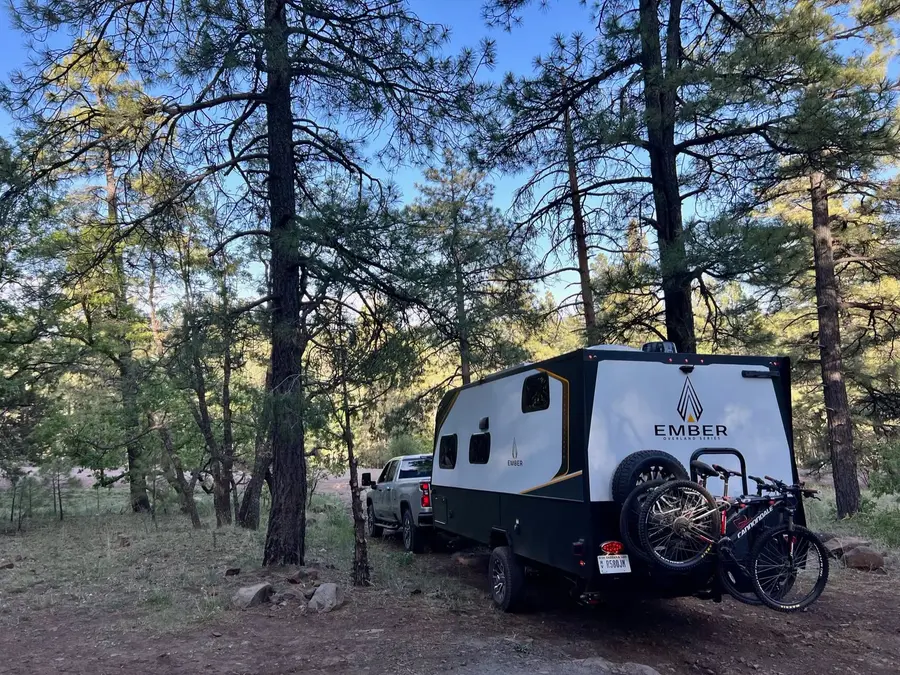 Ember Overland travel trailer with mountain bikes parked at a pine forest campsite