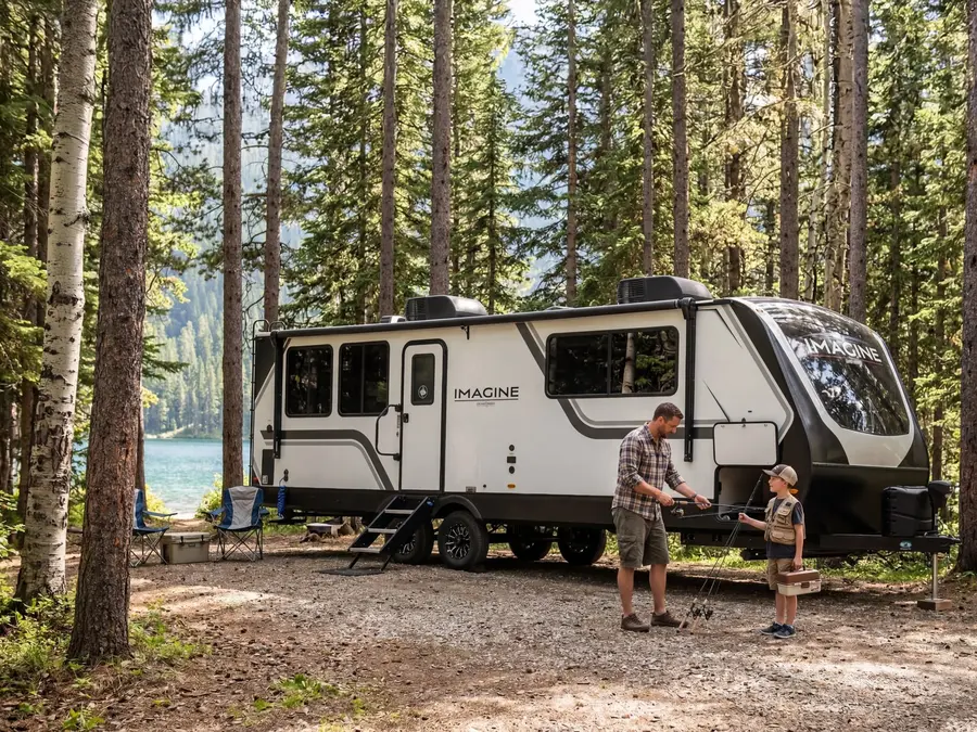 Father and son getting fishing rods ready beside a Grand Design Imagine travel trailer at a lakeside forest campsite