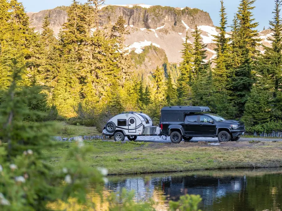 nuCamp TAG teardrop camper towed by a pickup truck through mountain scenery